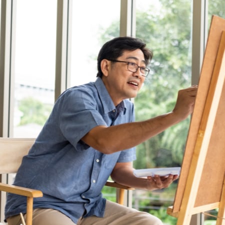 Mature man sitting in a chair painting on easel