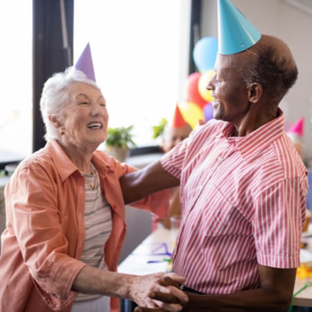 A mature woman and man, friends, wearing birthday hats and smiling